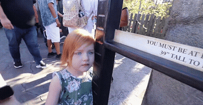 A Little Girl Is Standing Next To A Sign That Says You Must Be At 39 Inches Tall GIF