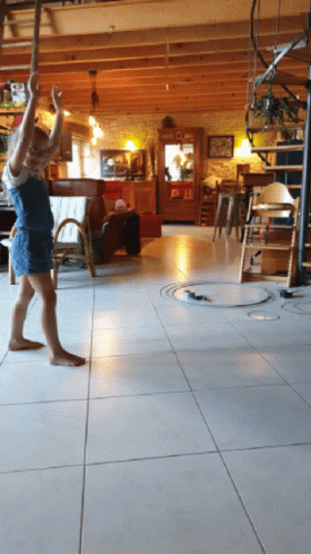 A Little Girl Is Standing On A Tiled Floor In A Living Room With A Spiral Staircase In The Background GIF
