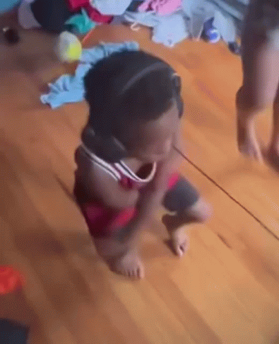 A Little Girl Is Standing On A Wooden Floor Looking At Herself In A Mirror . GIF