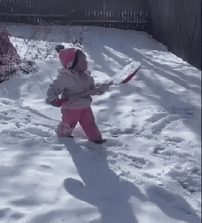 A Little Girl Is Walking Through The Snow While Holding A Shovel . GIF