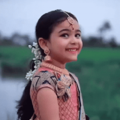 A Little Girl Is Wearing A Pink Dress And Smiling . GIF