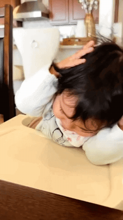 A Little Girl Laying On A Table With Her Head Resting On A Pillow GIF