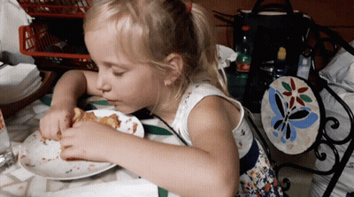 A Little Girl Sits At A Table With A Plate Of Food GIF