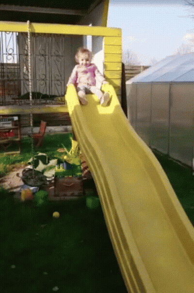 A Little Girl Sits On A Yellow Slide GIF