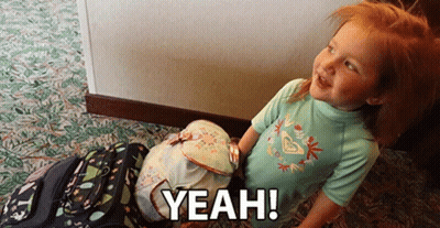 A Little Girl Standing Next To A Stack Of Backpacks With The Words Yeah Written On It GIF