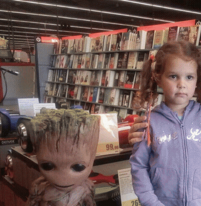 A Little Girl Stands Next To A Statue Of Groot In A Book Store GIF
