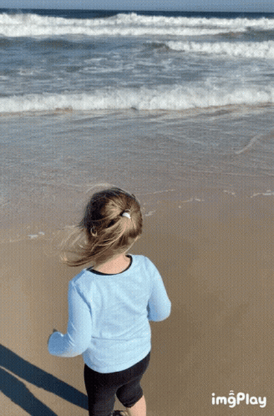 A Little Girl Stands On A Beach Looking At The Ocean With Imgplay At The Bottom GIF