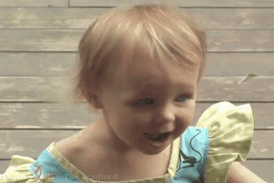 A Little Girl Wearing A Blue And Yellow Dress Is Smiling . GIF
