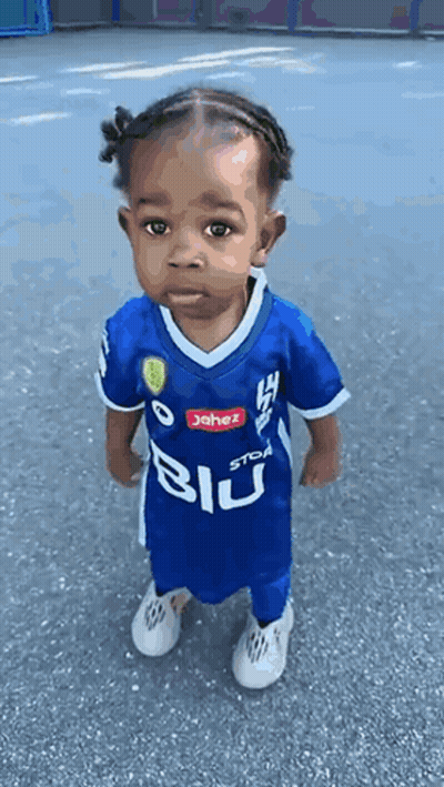 A Little Girl Wearing A Blue Soccer Jersey Is Standing On The Street . GIF