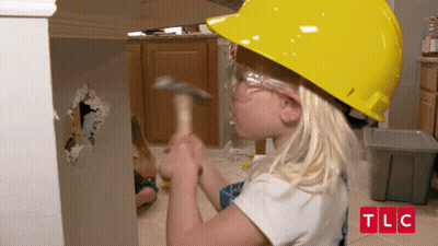A Little Girl Wearing A Hard Hat And Goggles Is Hitting A Wall With A Hammer .. GIF