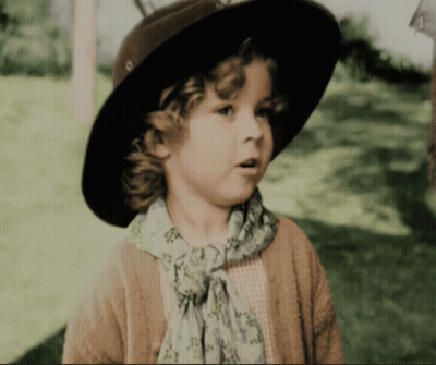 A Little Girl Wearing A Hat And Scarf Looks To The Side GIF