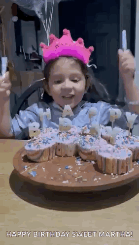 a little girl wearing a pink crown is eating cupcakes .
