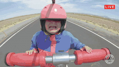 A Little Girl Wearing A Pink Helmet And A Blue Jacket Is Riding A Red Pipe On A Road With A Live Sign Above GIF