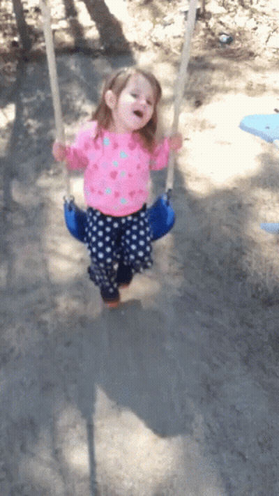 A Little Girl Wearing A Pink Shirt And Blue Polka Dot Pants Is Swinging On A Blue Swing GIF