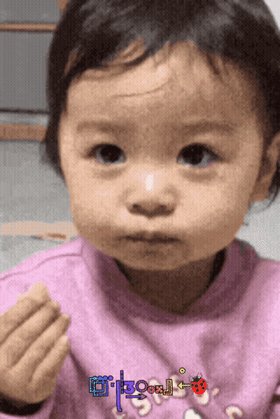A Little Girl Wearing A Pink Sweater With A Ladybug On It Looks At The Camera GIF