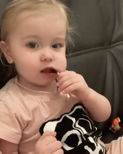 A Little Girl Wearing A Shirt With A Skull On It Eating A Lollipop GIF