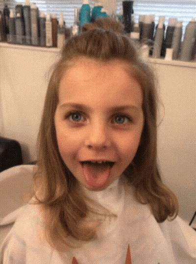 A Little Girl Wearing A White Cape With A Unicorn On It Sticks Out Her Tongue GIF