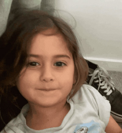 A Little Girl Wearing A White Shirt With A Picture Of A Horse On It Looks At The Camera GIF