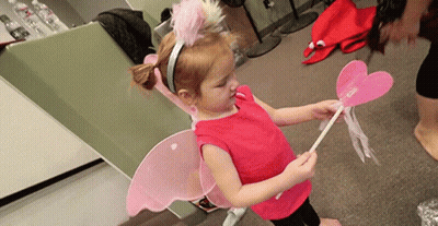 A Little Girl Wearing Fairy Wings And A Headband Holds A Pink Wand GIF