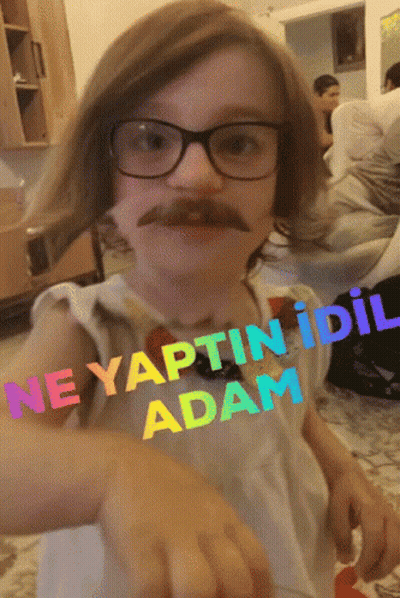 A Little Girl Wearing Glasses And A Fake Mustache Has The Words Ne Yaptin Idil Adam Written On Her Shirt GIF
