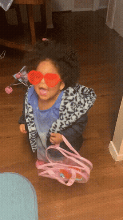 A Little Girl Wearing Heart Shaped Sunglasses And Holding A Pink Bag GIF