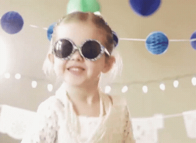 A Little Girl Wearing Sunglasses And A Party Hat Is Dancing At A Birthday Party . GIF