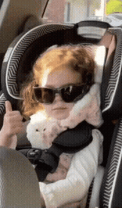 A Little Girl Wearing Sunglasses Is Sitting In A Car Seat GIF