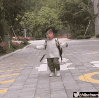 A Little Girl With A Backpack Is Walking Down A Brick Road .. GIF