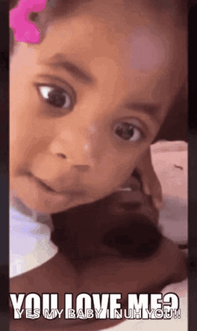 A Little Girl With A Pink Flower In Her Hair Is Looking At The Camera With A Caption That Says You Love Me ? GIF