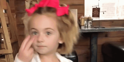 A Little Girl With A Red Bow In Her Hair Is Making A Face . GIF
