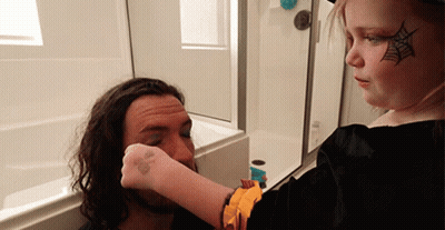 A Little Girl With A Spider Web Painted On Her Face Is Applying Makeup To A Man 'S Face GIF