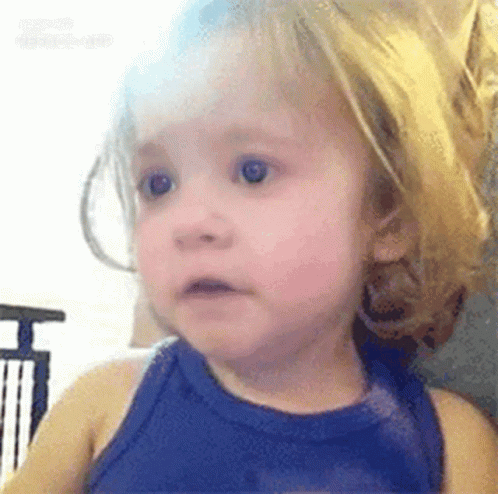 A Little Girl With Blonde Hair Is Wearing A Blue Tank Top And Making A Surprised Face . GIF