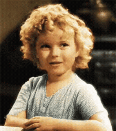 A Little Girl With Curly Blonde Hair Is Wearing A Blue Shirt GIF