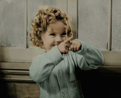 A Little Girl With Curly Hair Is Pointing Her Finger At Something GIF