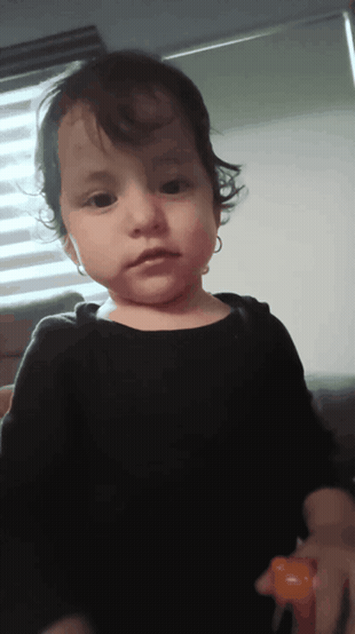 A Little Girl With Curly Hair Is Wearing A Black Shirt And Earrings GIF