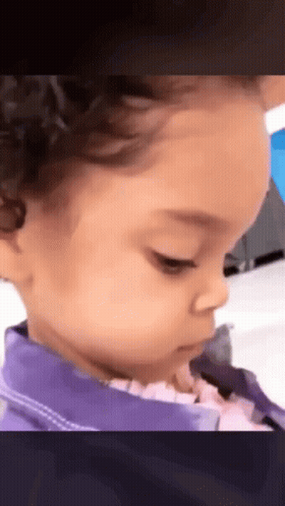 A Little Girl With Curly Hair Is Wearing A Purple Jacket And Looking At The Camera . GIF