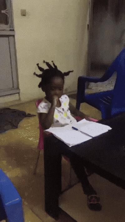 A Little Girl With Dreadlocks Sits At A Table With A Pen In Her Hand GIF