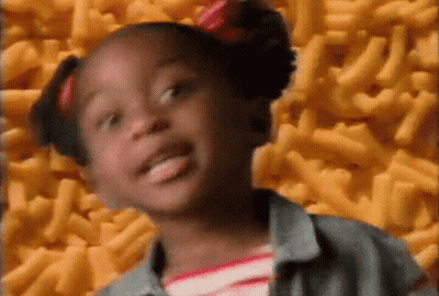 A Little Girl With Pigtails Is Standing In Front Of A Pile Of Macaroni And Cheese . GIF