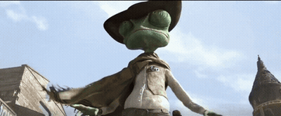 A Lizard Wearing A Cowboy Hat And Cape Is Standing In Front Of A Building GIF