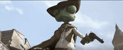A Lizard Wearing A Cowboy Hat And Cape Stands In Front Of A Building GIF