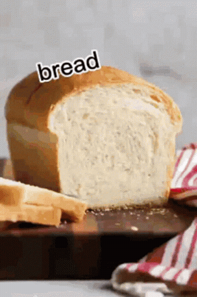 A Loaf Of Bread Is Sitting On A Wooden Cutting Board With A Knife . GIF