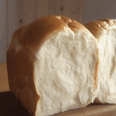 A Loaf Of Bread That Has Been Cut In Half Sits On A Wooden Table GIF