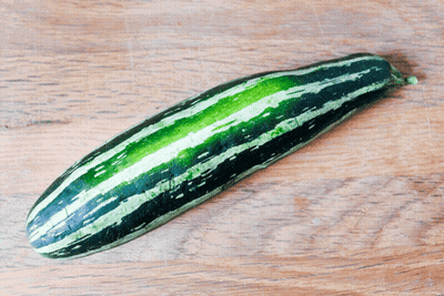 A Long Green And Black Striped Zucchini On A Wooden Table GIF