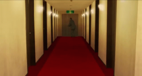 A Long Hallway With A Red Carpet And A Sign That Says Exit On It GIF