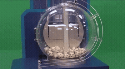 A Lottery Machine Filled With Balls And A Green Background GIF