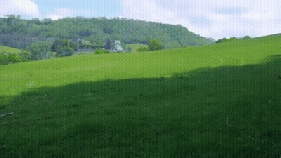 A Lush Green Field With A House On The Hill In The Background GIF