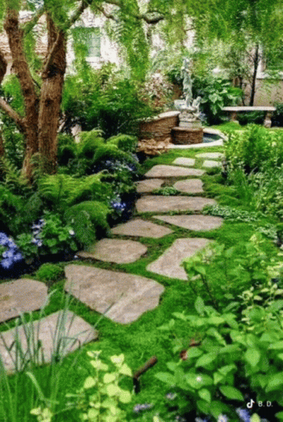 A Lush Green Garden With A Stone Path And A Statue GIF