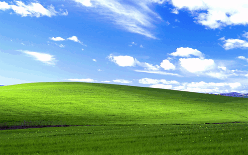 A Lush Green Hillside With A Blue Sky And White Clouds GIF