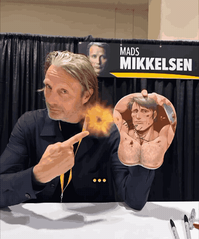 A Mads Mikkelsen Sign Hangs Above A Man 'S Arm GIF