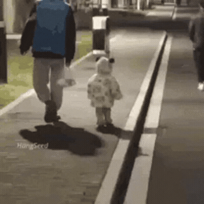 A Man And A Baby Are Walking Down A Sidewalk At Night . GIF